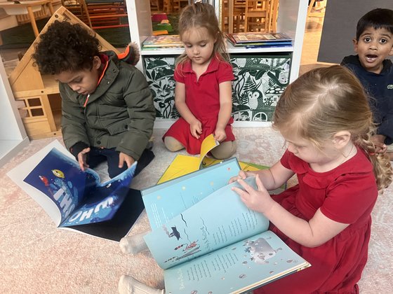 Three Selwyn students sharing a large picture book on the classroom floor